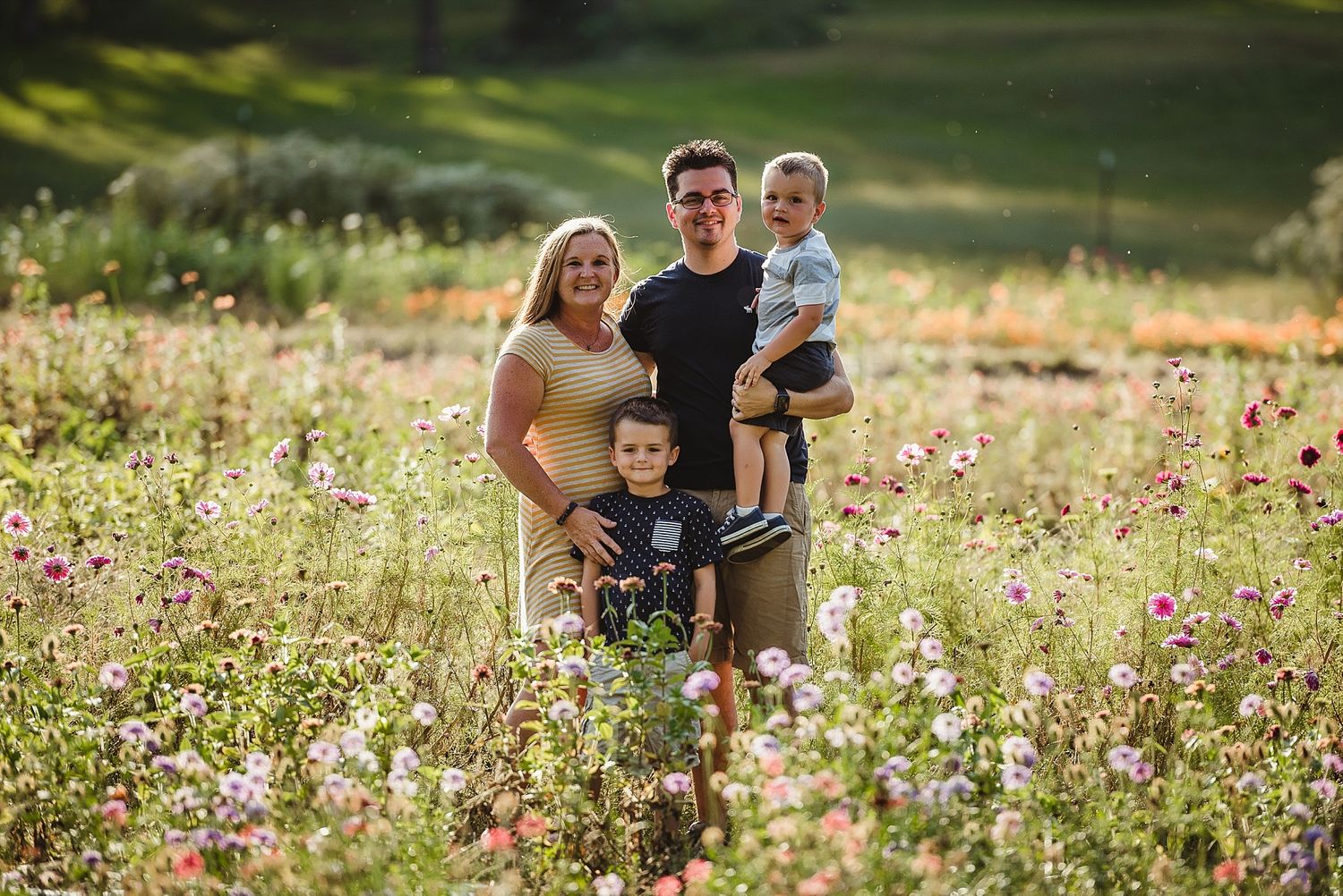 Family standing together in a blooming wildflower meadow at sunset.