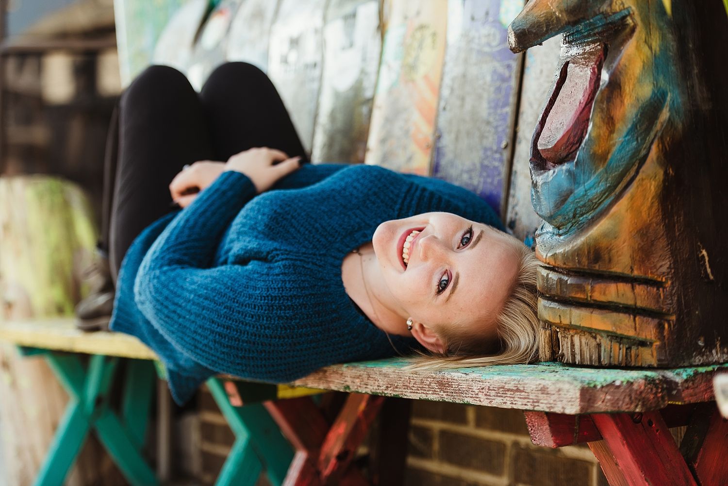 Person in blue sweater lying on colorful painted bench outdoors.