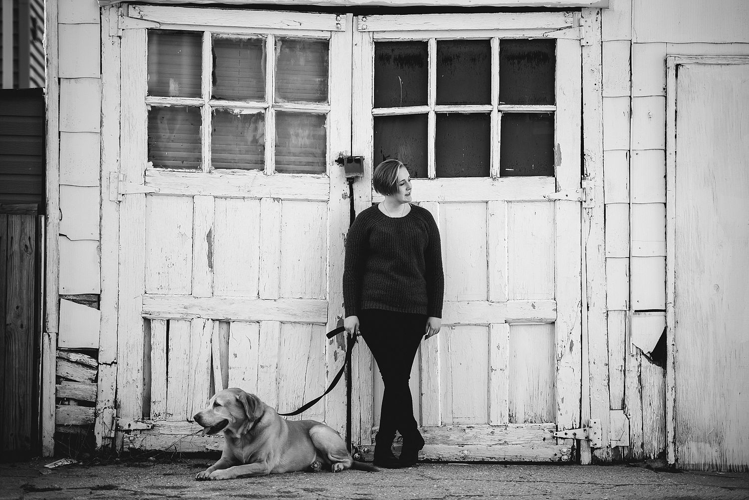 Black and white portrait of person with dog in front of weathered door.