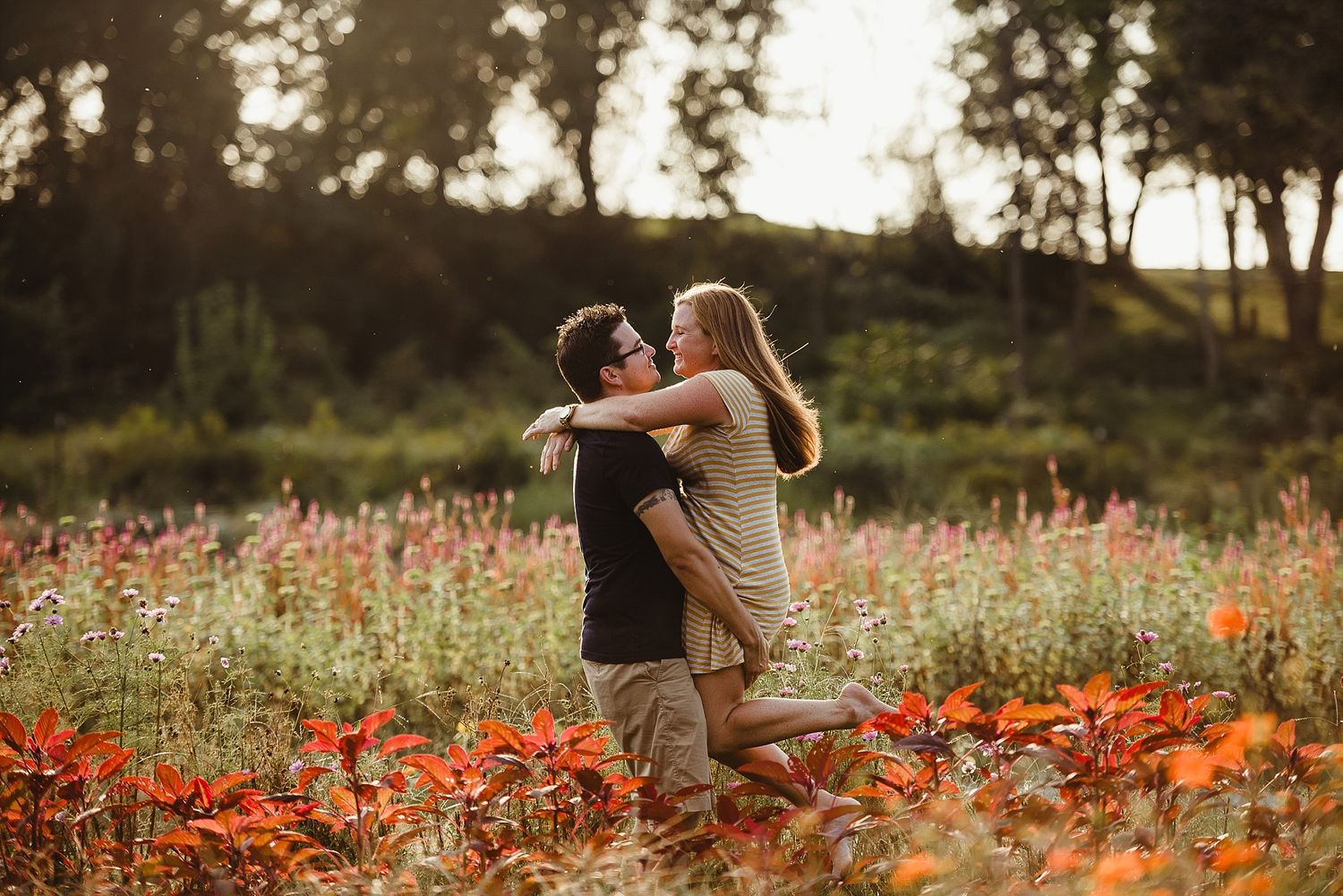 Couple embracing in field of orange wildflowers at sunset.