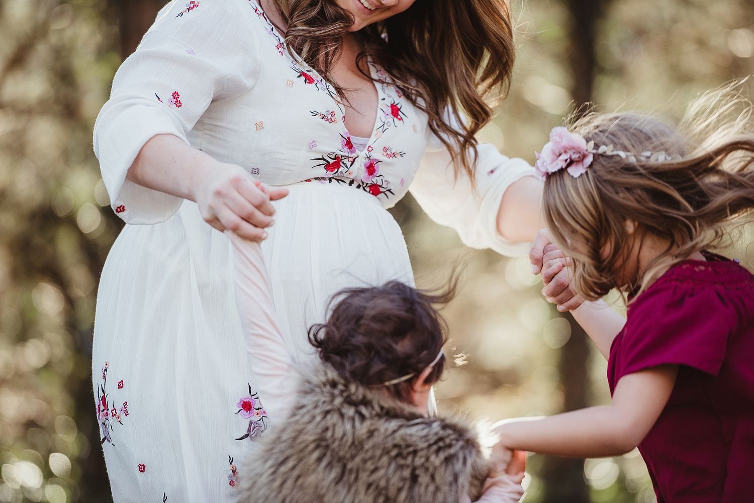 Maternity moment captured outdoors with floral dress and burgundy accents.
