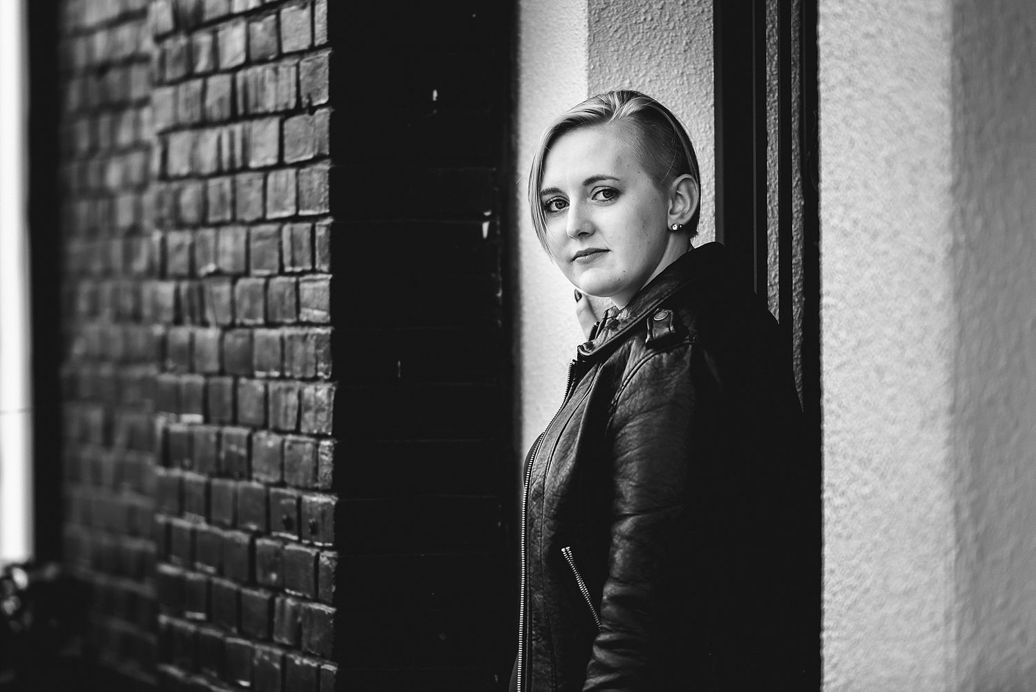 Dramatic black and white portrait against brick wall showing contemplative expression and leather jacket.