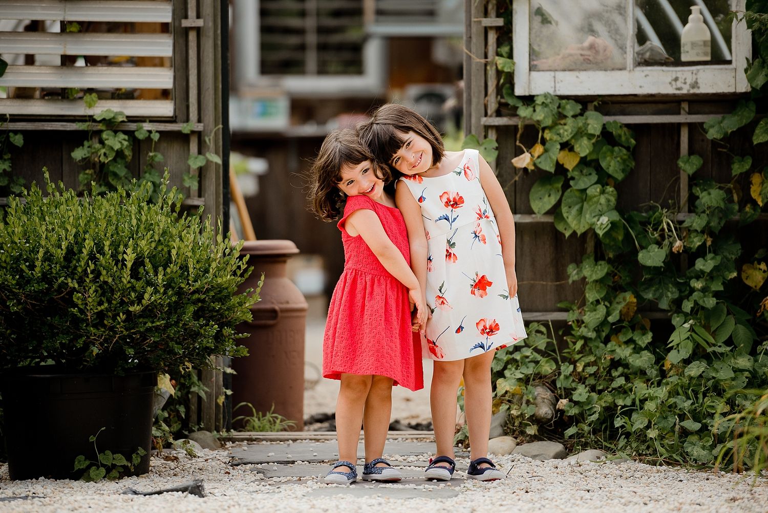 Two children in summer dresses share a sweet moment together in a garden setting.