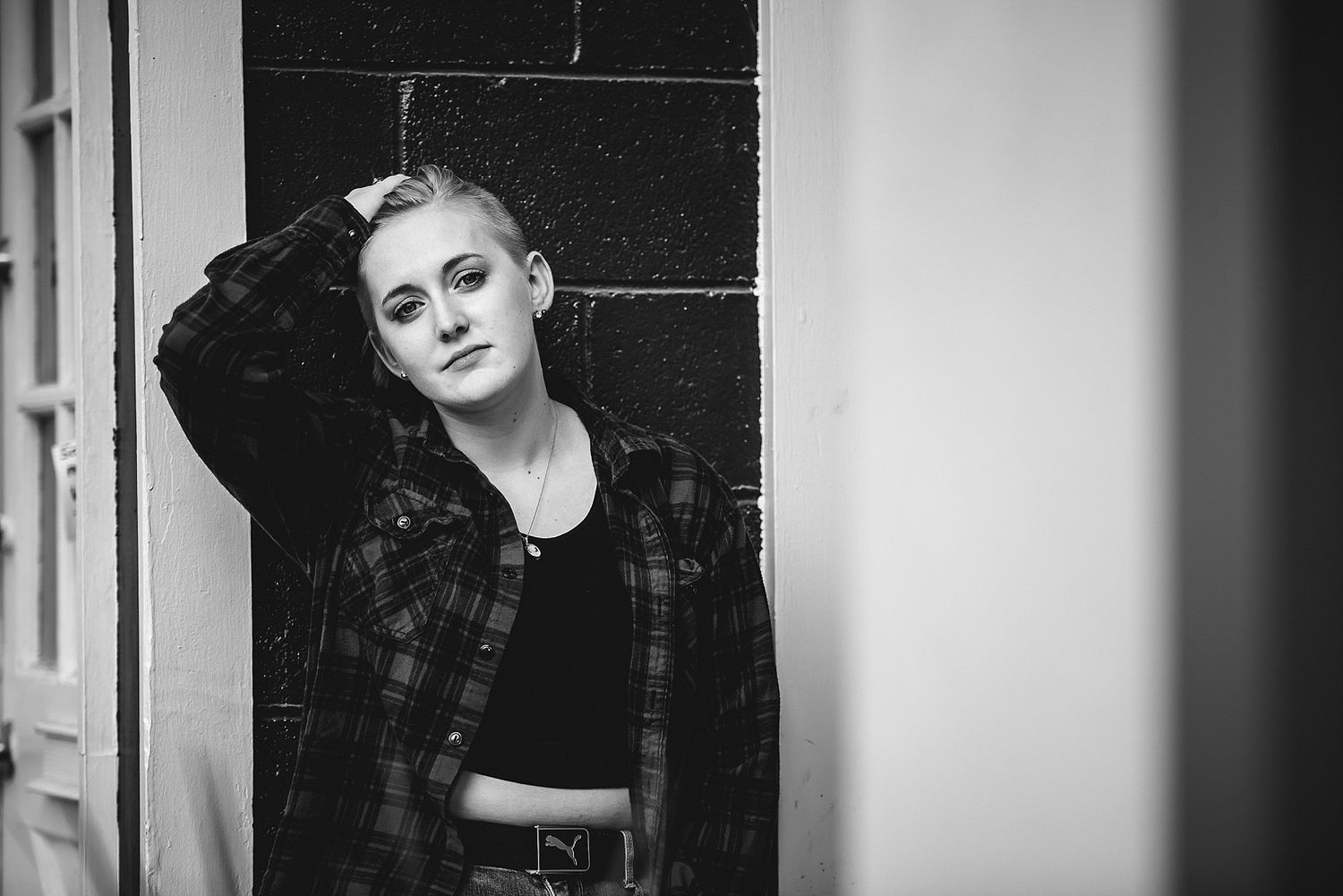Moody black and white portrait against brick wall showing casual style and artistic composition.
