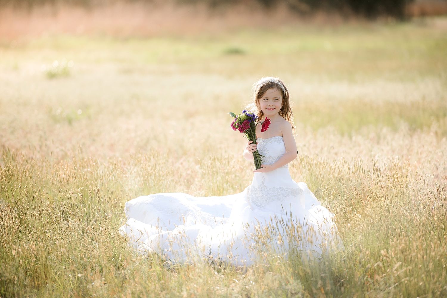 Ethereal bridal portrait in a sunlit meadow with flowing white dress and delicate flowers.