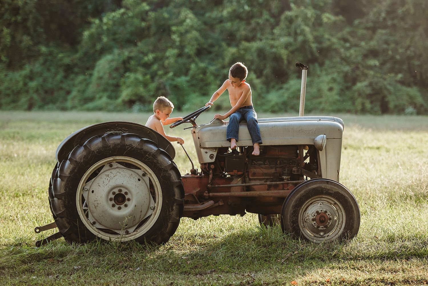 Children playing on vintage tractor in golden summer field during sunset.