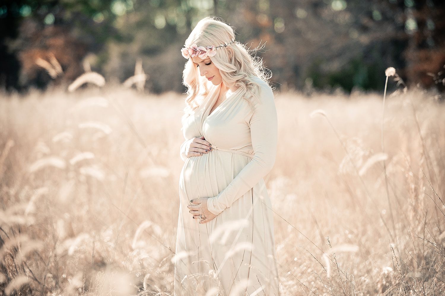 Dreamy maternity portrait in flowing dress amid tall grass during golden hour.
