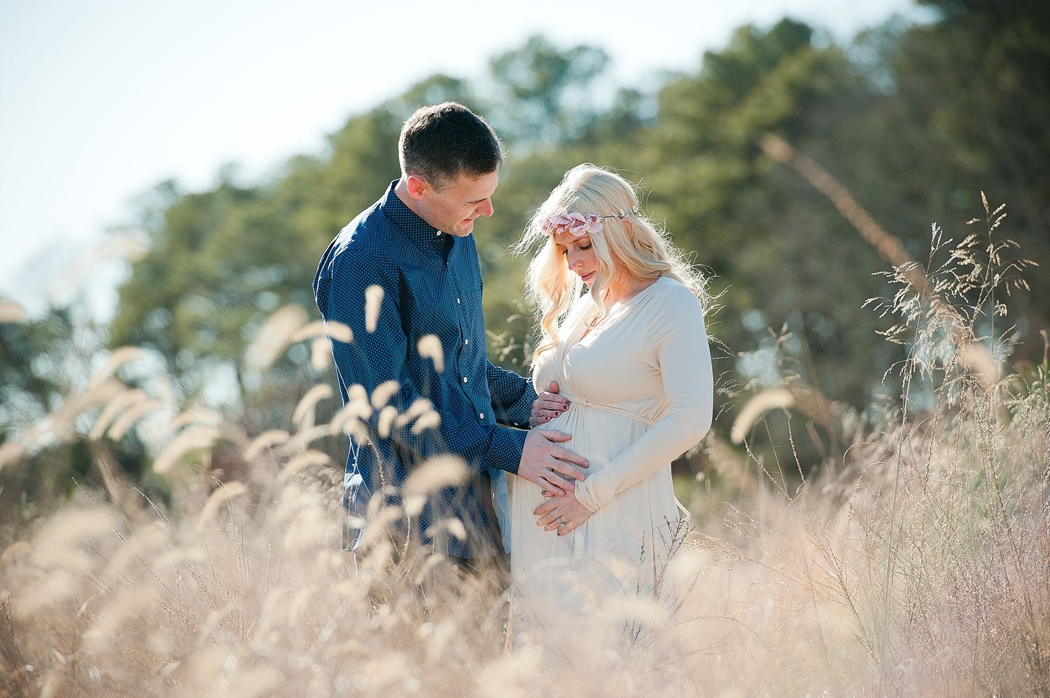 A romantic maternity photo shoot in a field of tall grass at sunset.