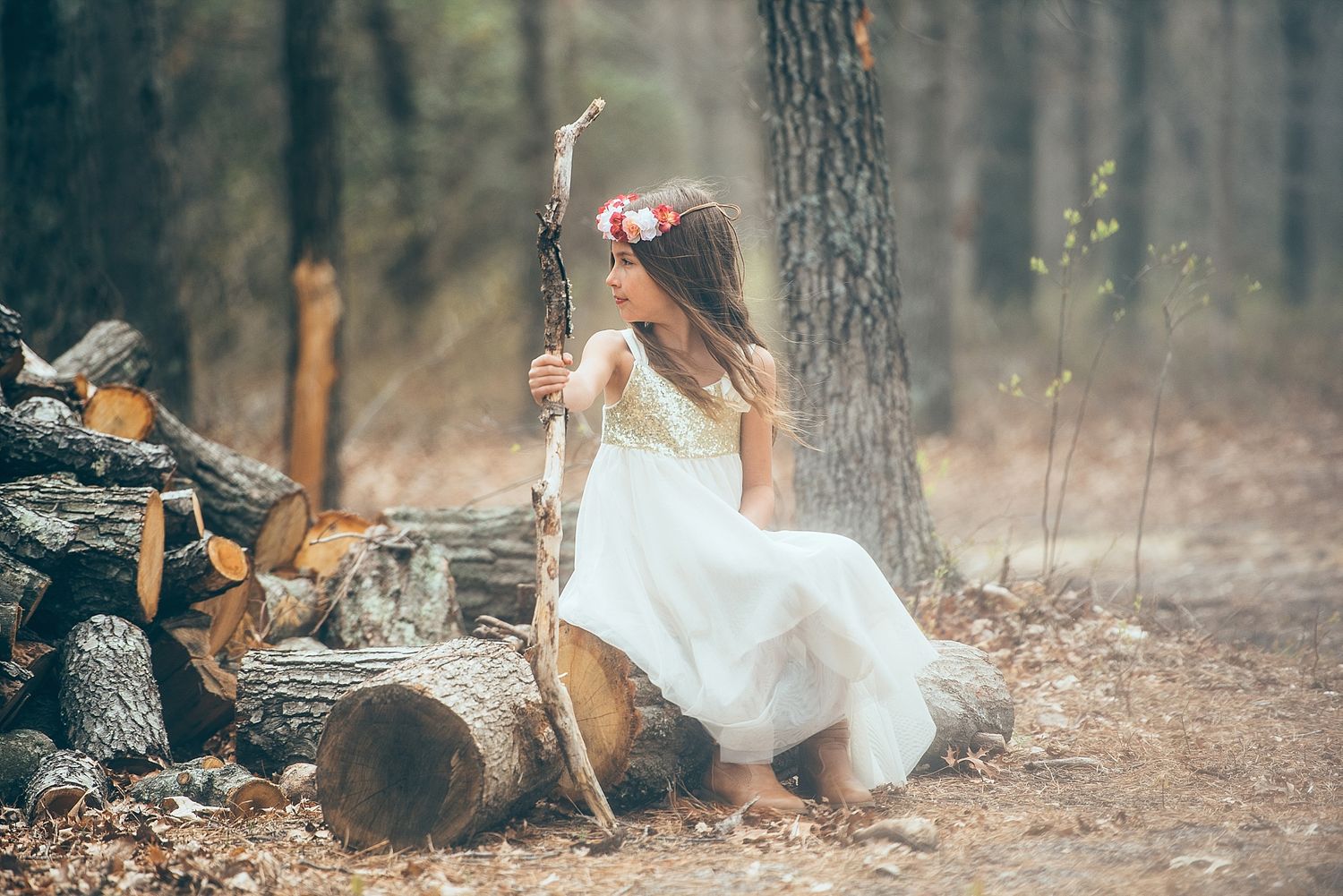 A whimsical portrait of someone in a white dress sitting on logs in a forest setting.