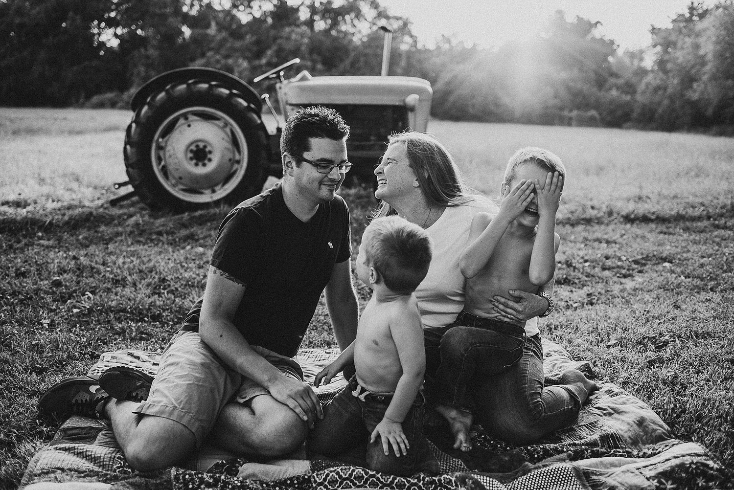 A casual family picnic scene near a vintage tractor in black and white.