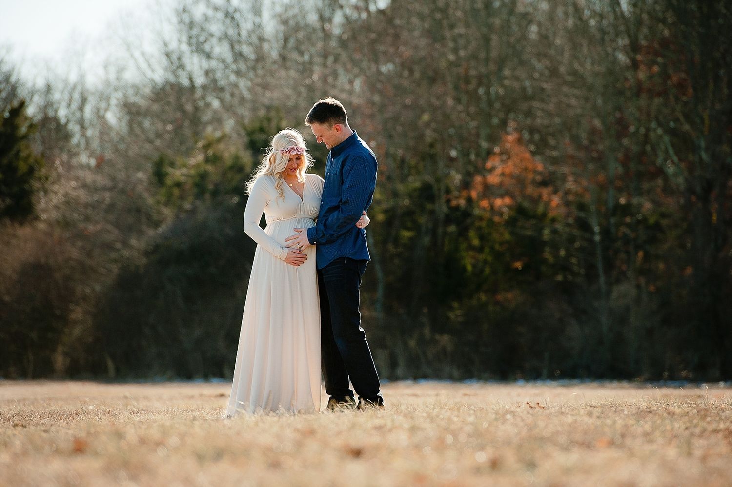A couple in wedding attire standing in an autumn field during golden hour.