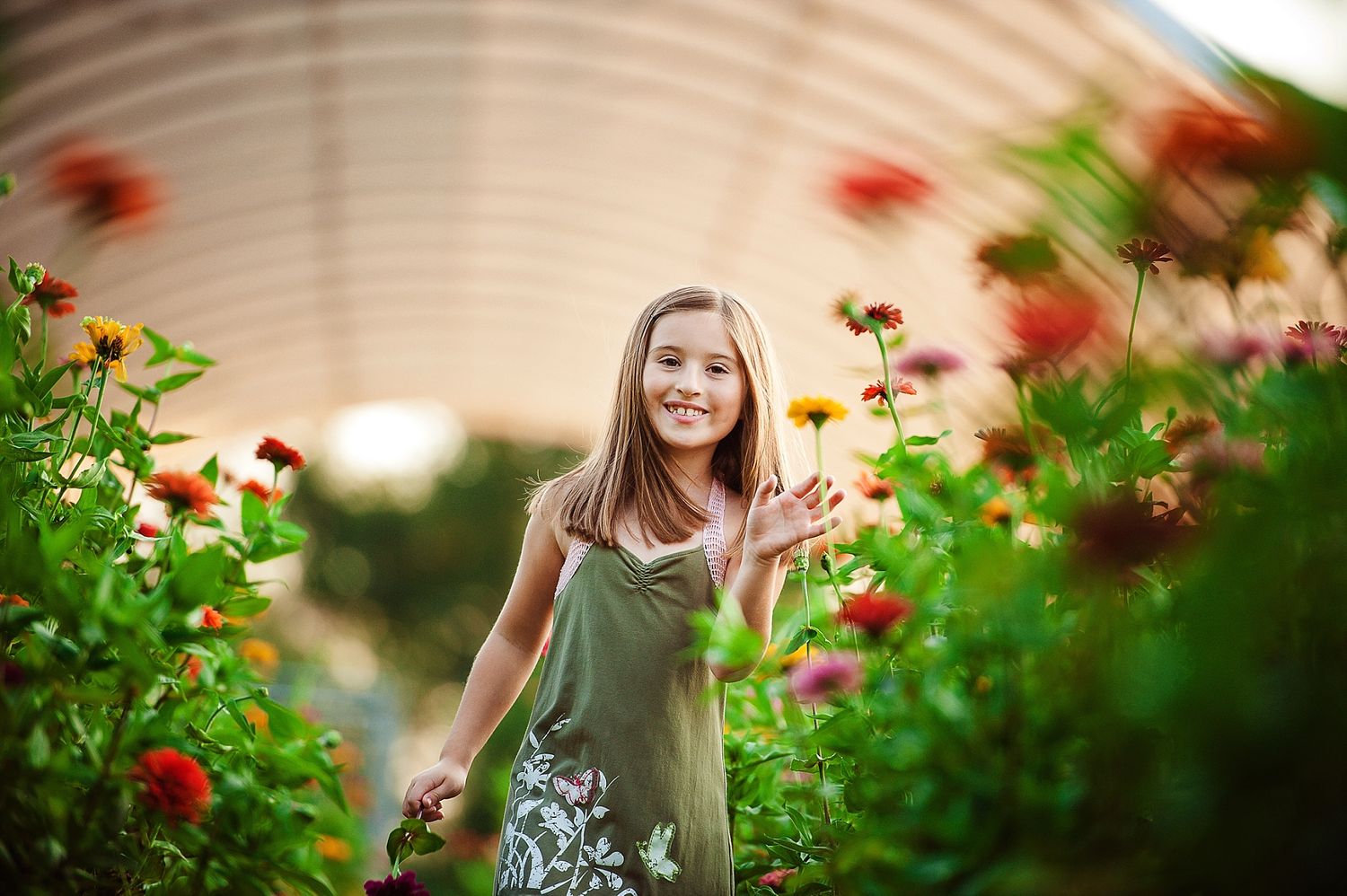 A person in a green dress stands among blooming flowers in a garden setting.