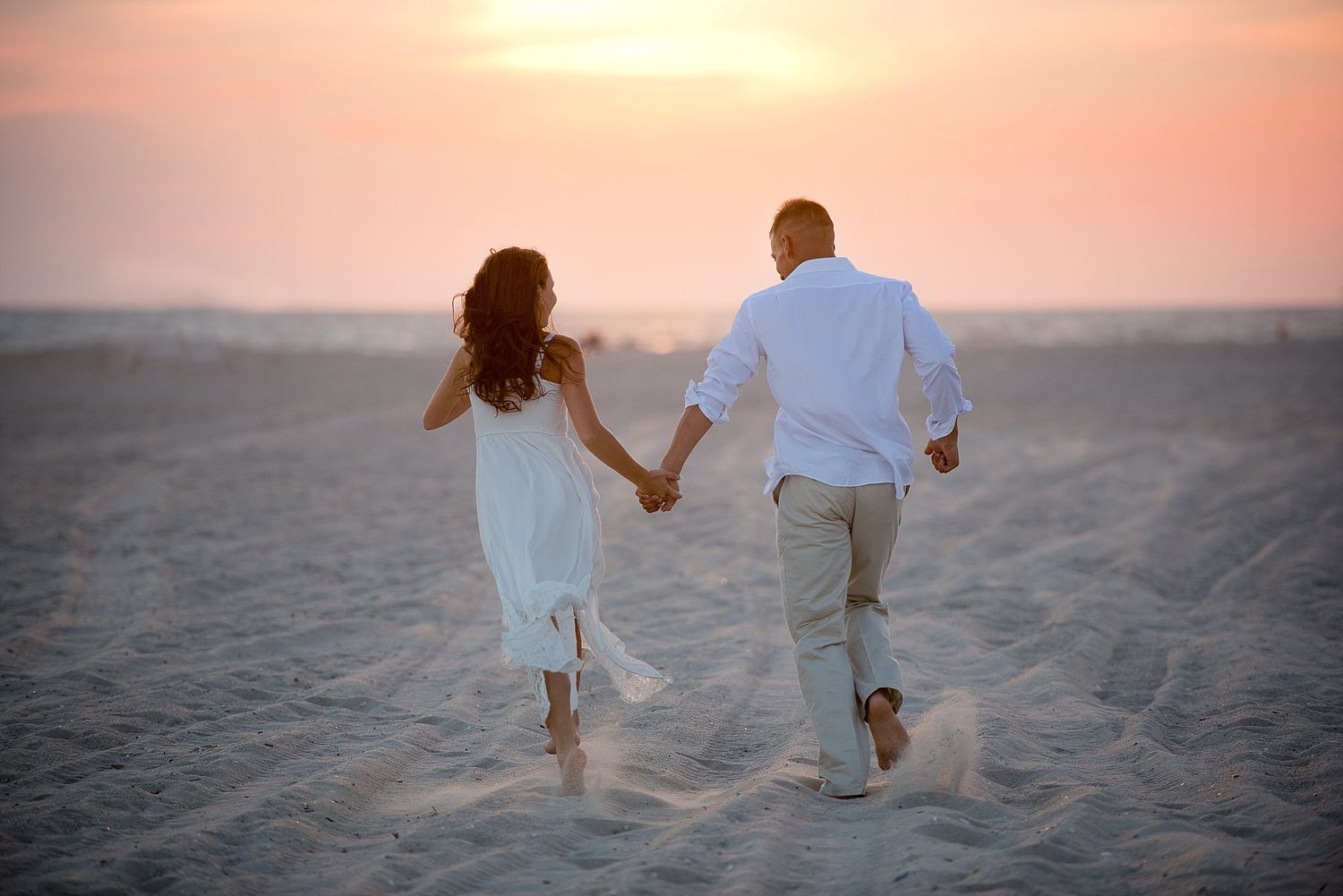 Silhouetted couple runs hand in hand on beach during golden sunset.