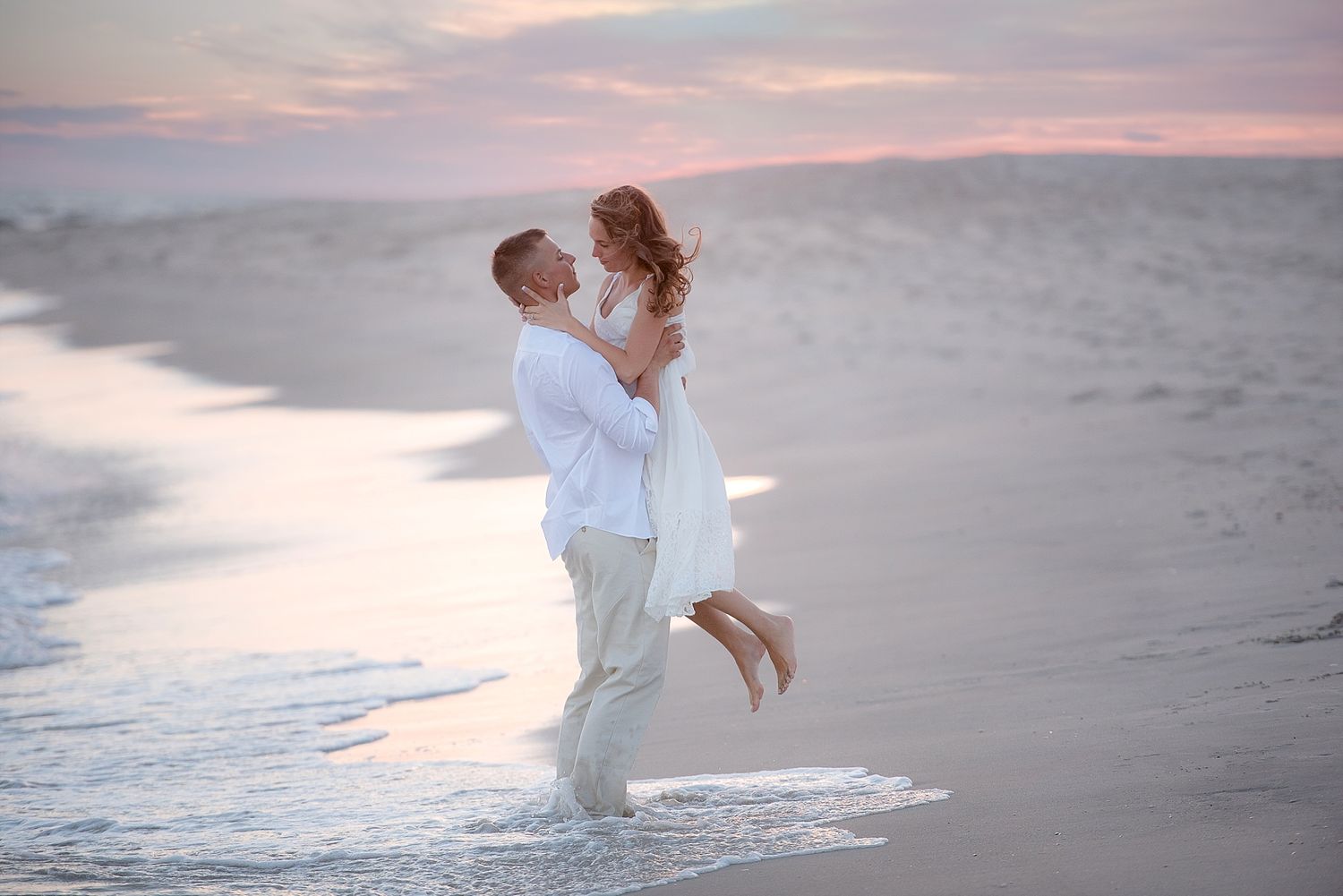 Romantic couple embracing on beach at sunset with waves in background.