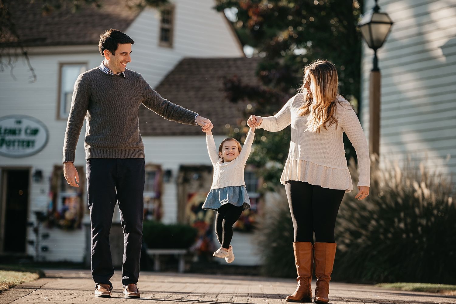 A family lifts and swings a small child while walking together on a sunny day.