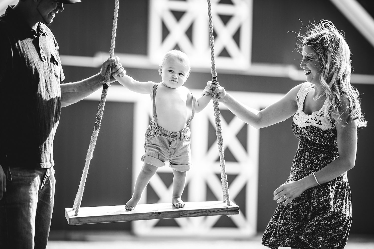 Child on swing being supported by adults in black and white photograph.