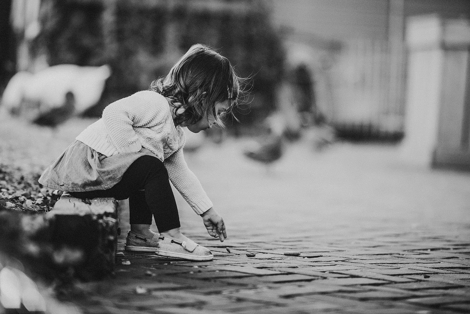 Child in black and white photo playing with water at the edge of a pond.