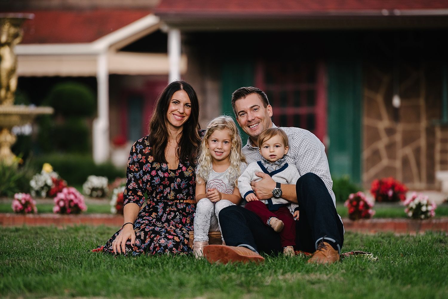 Family sitting together on grass in front of house with red trim.