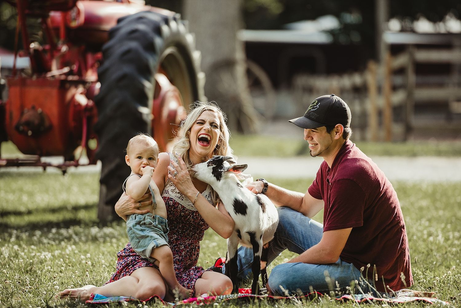 A joyful family moment outdoors with a baby and dog next to a red tractor.