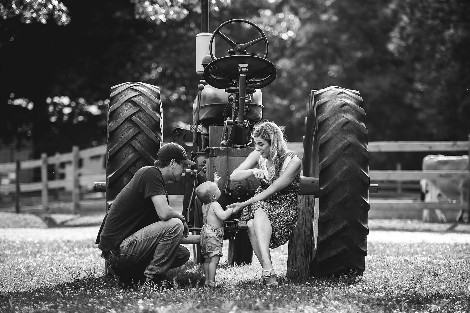A dramatic black and white portrait taken between large tractor tires on a farm.