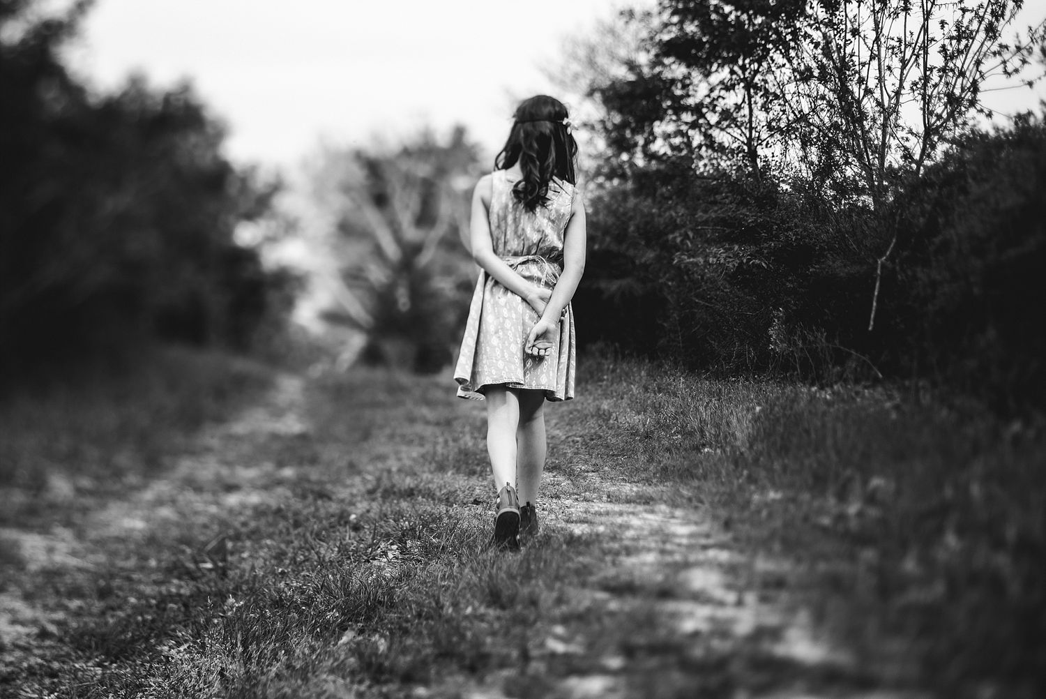 Woman in dress walking alone on rural path in black and white photograph.