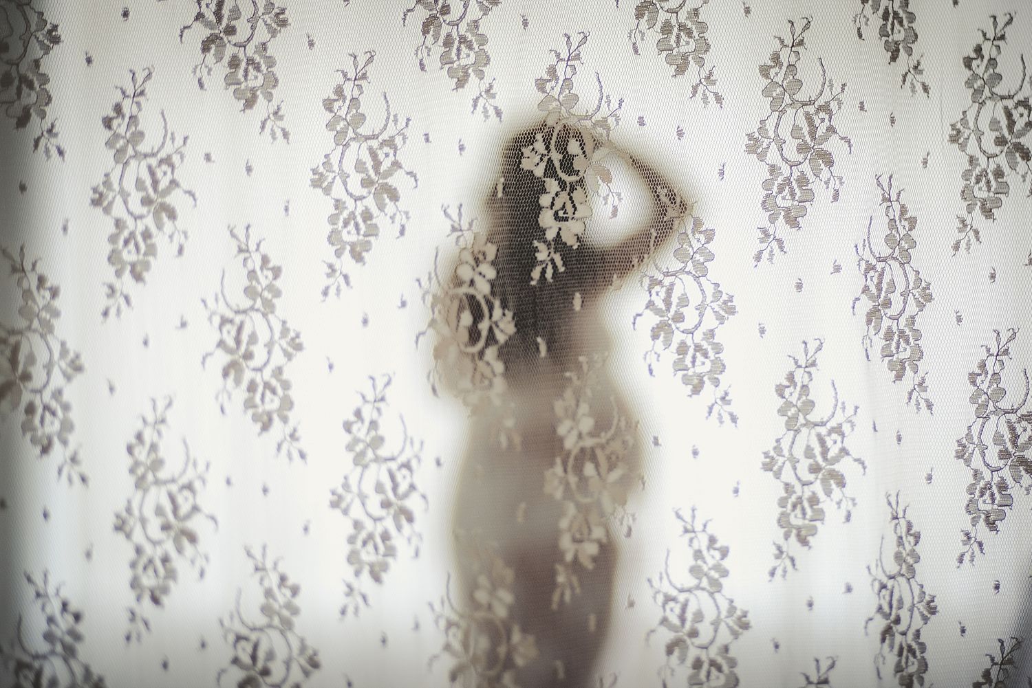 Silhouette behind sheer floral patterned curtains creates dreamy artistic effect.