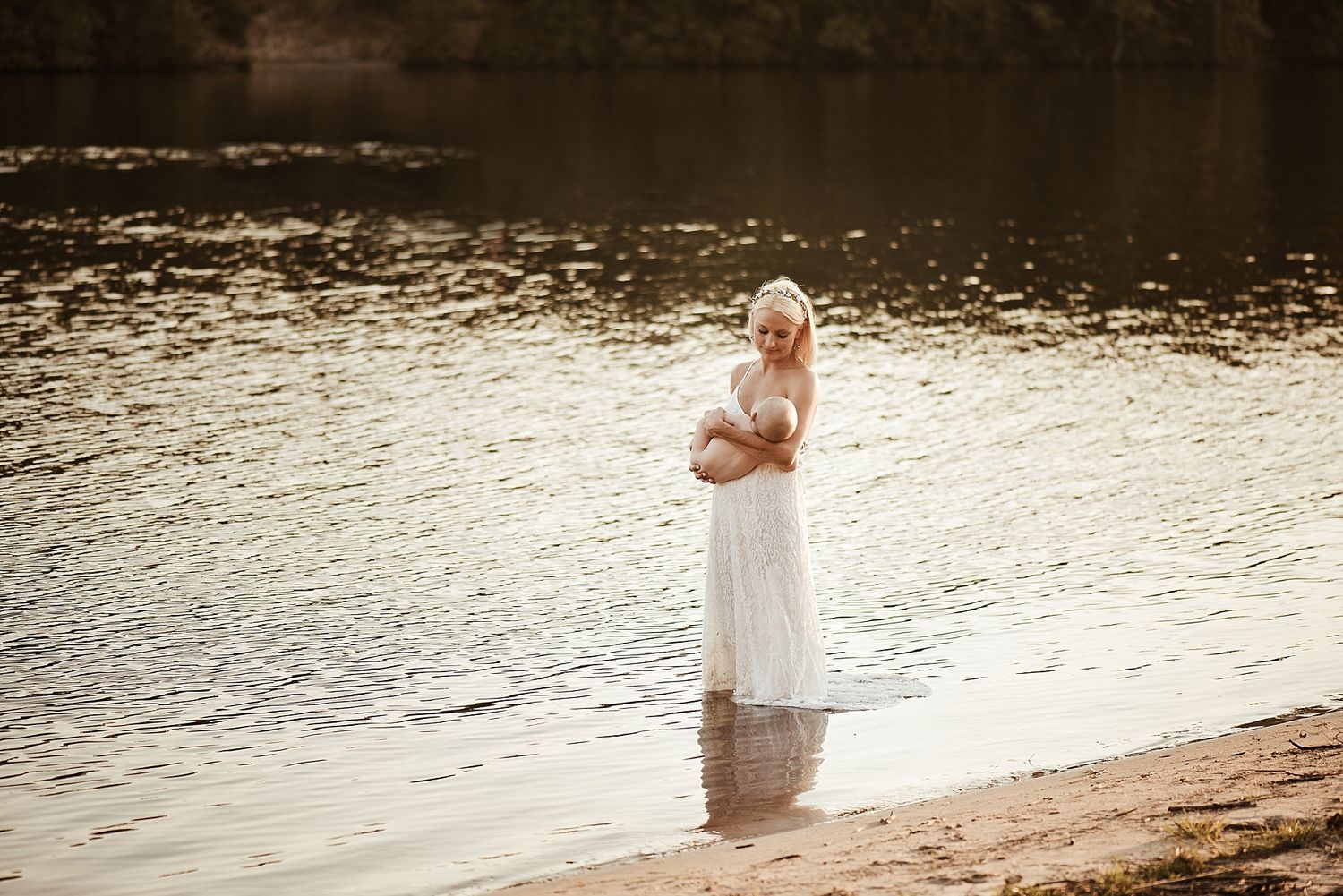 A person in flowing white dress stands at water's edge during golden hour.