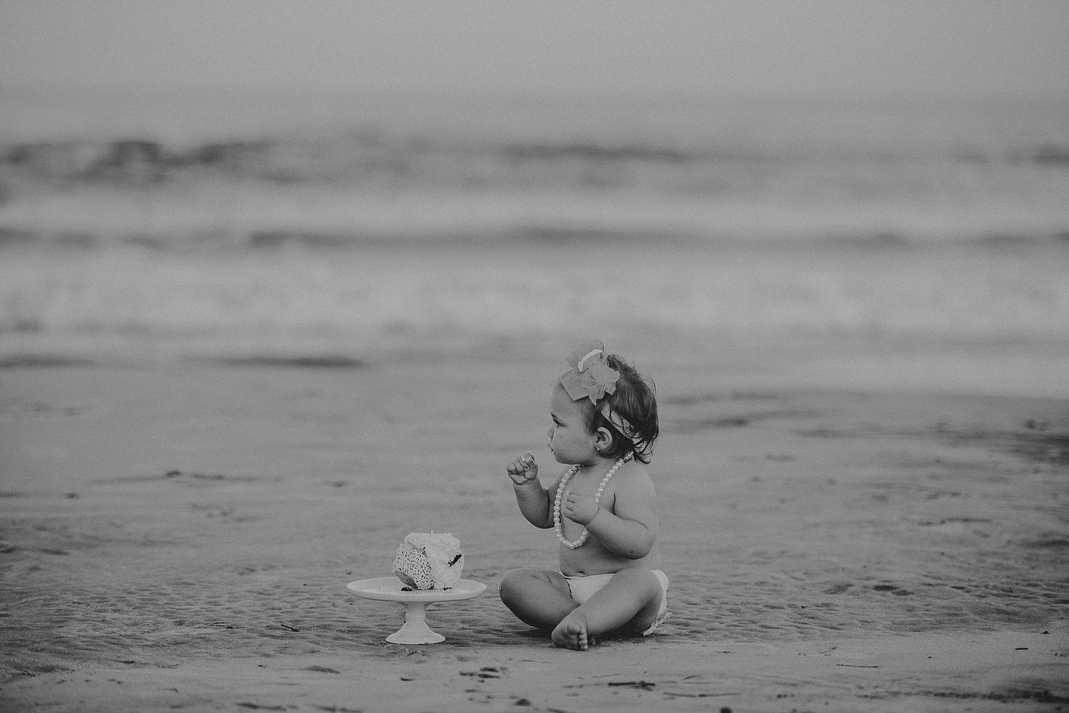 Black and white photo of small child playing in sand at the beach.