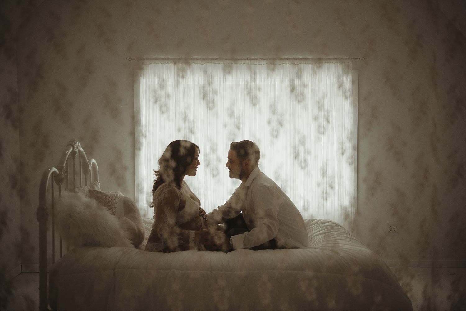 Romantic vintage-style photo of couple sitting together by window with lace curtains.