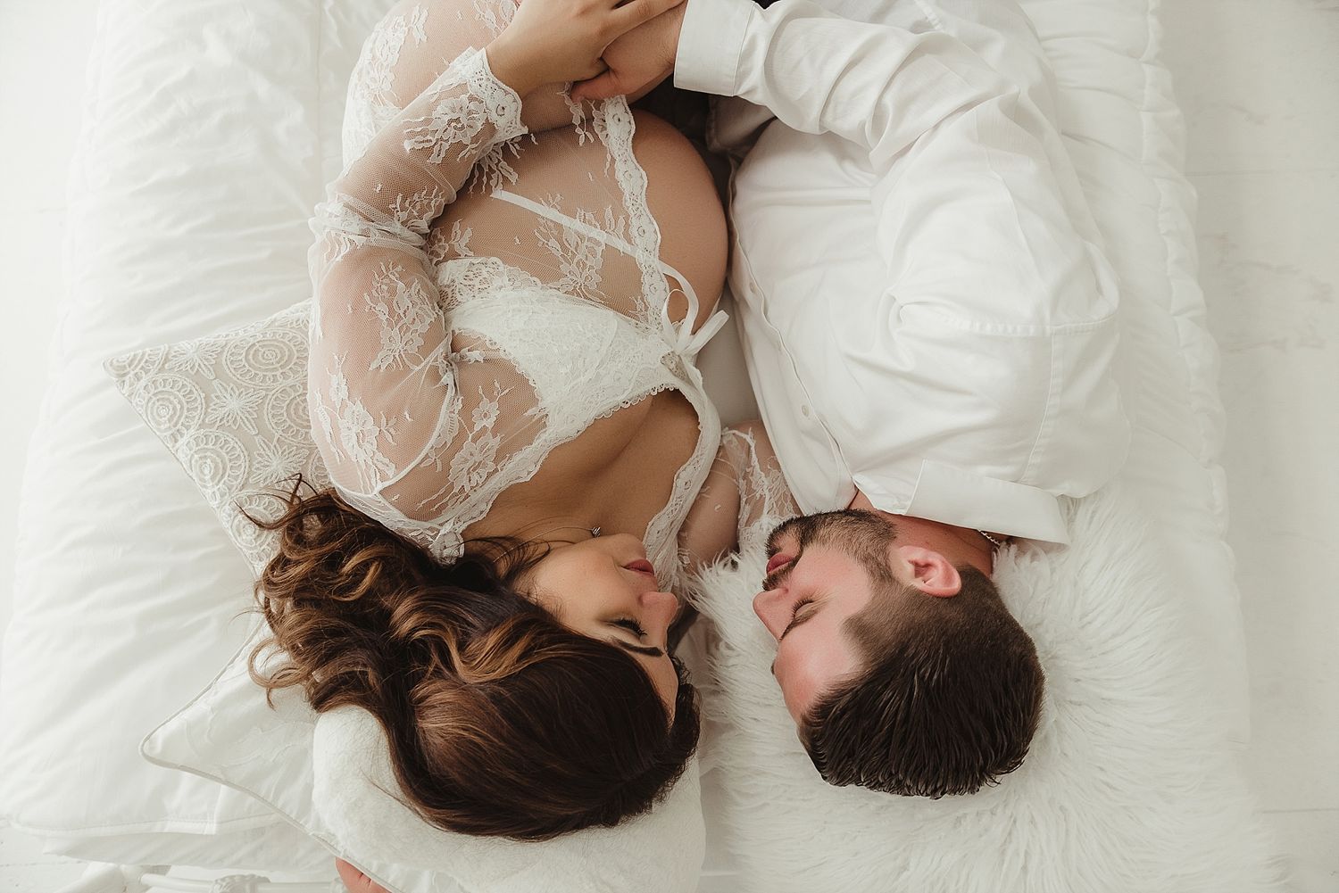 Overhead view of couple lying together on white bedding wearing lace.