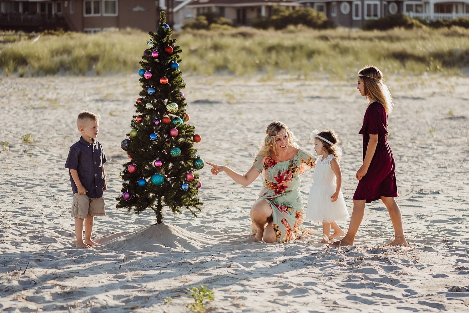 Family gathered around decorated Christmas tree on beach at sunset.