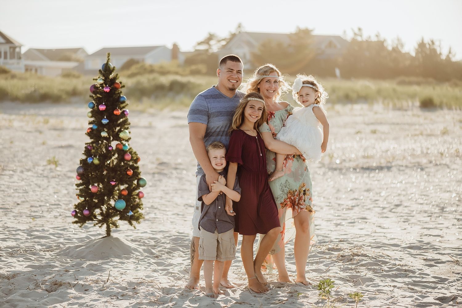 Family portrait on beach with decorated Christmas tree at golden hour.