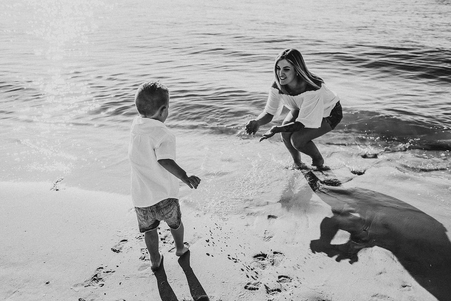 Black and white photo of two people playing on beach near ocean.