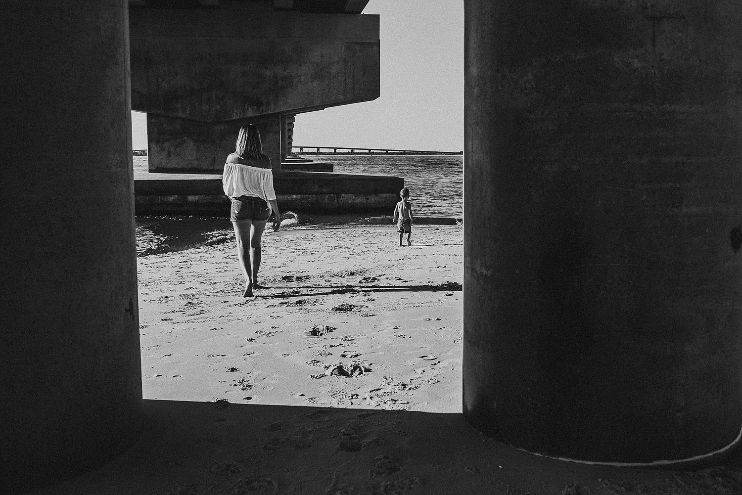 Black and white image of silhouettes walking under bridge structure.