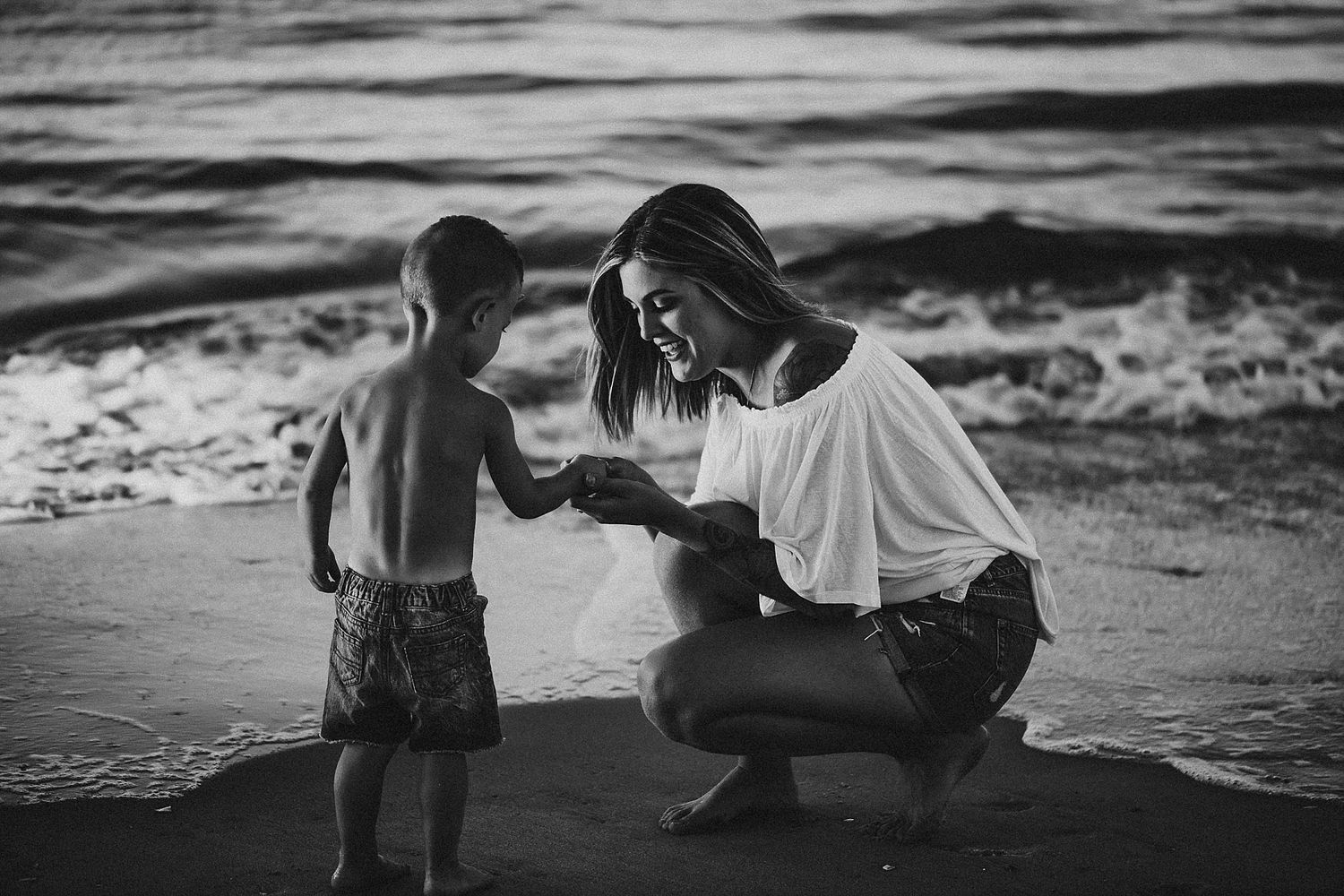 Black and white photo of mother and child bonding at beach during sunset.