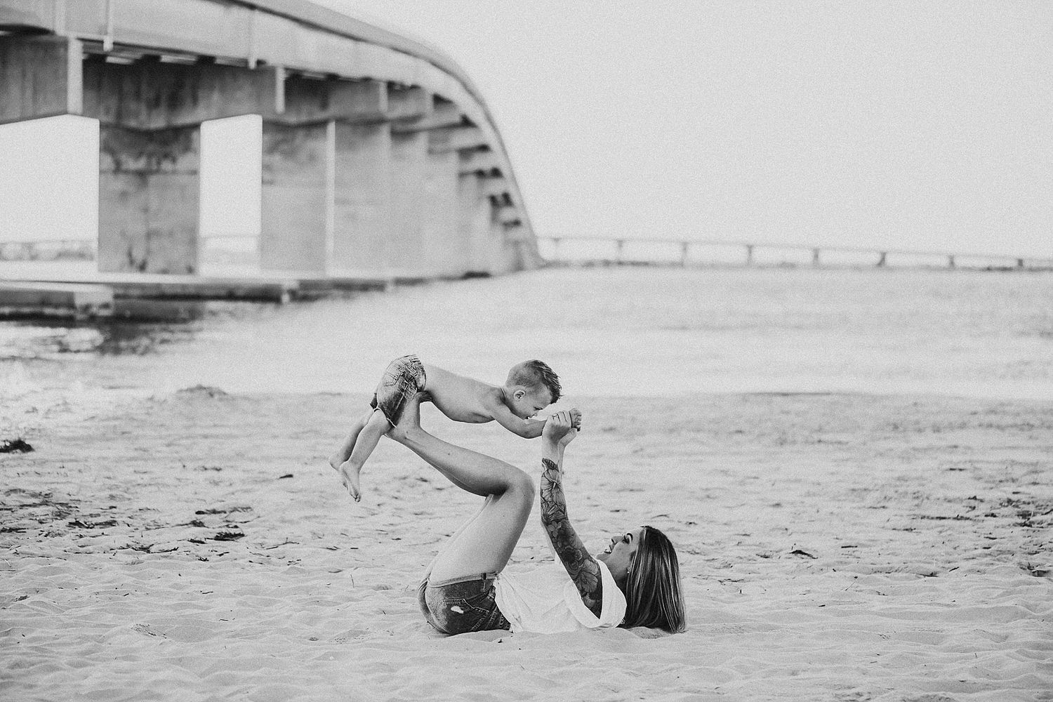 Black and white photo of playful moment under bridge at beach.