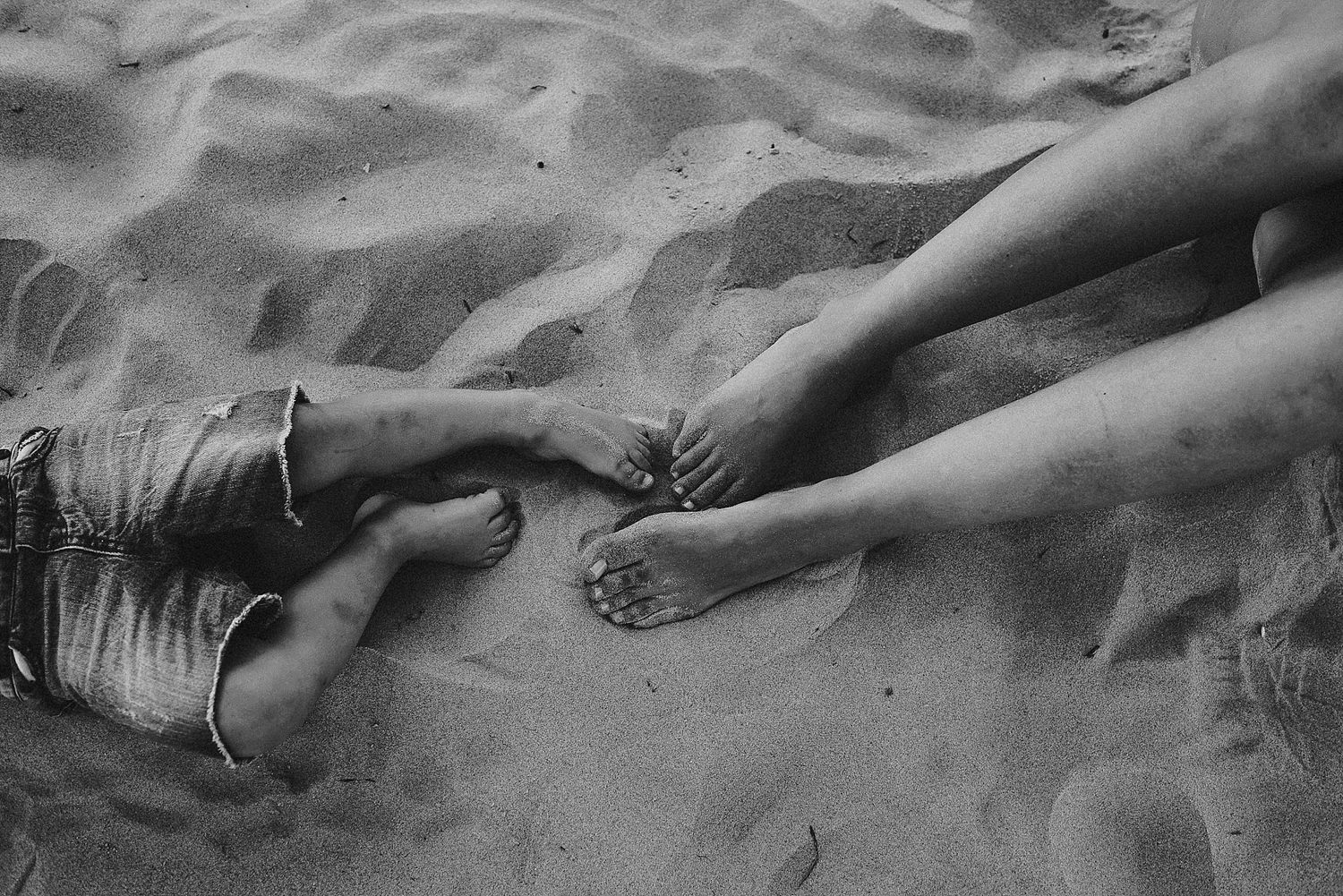 Black and white photo of hands reaching toward each other on sandy beach.