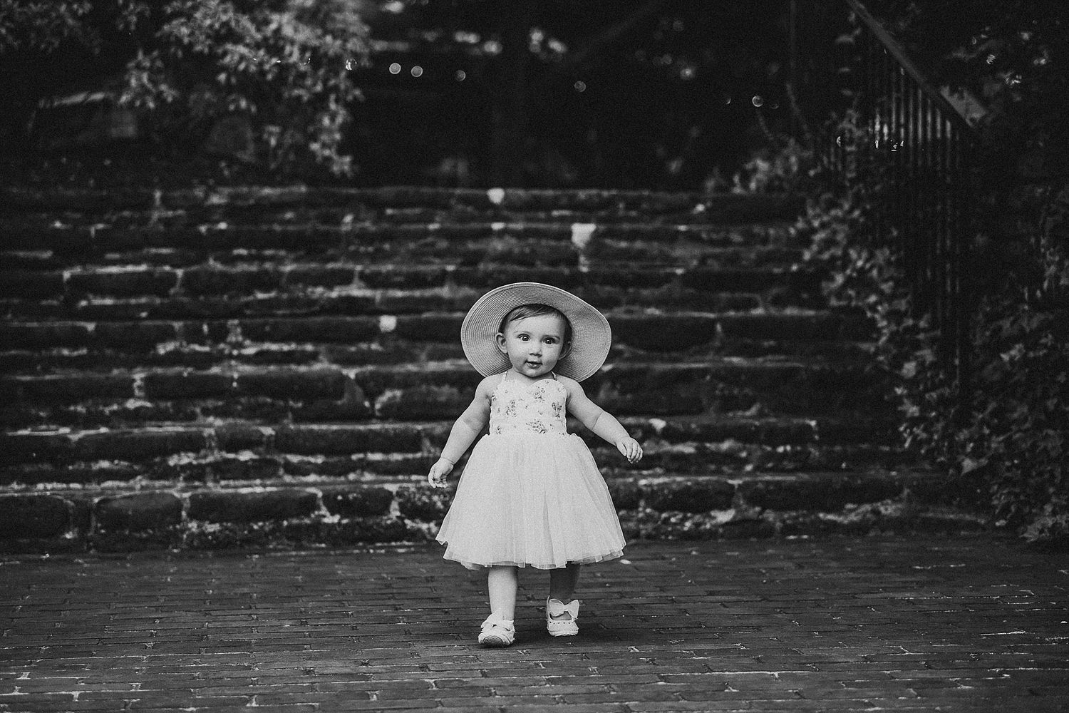 Black and white photo of toddler in white dress standing on stone steps.