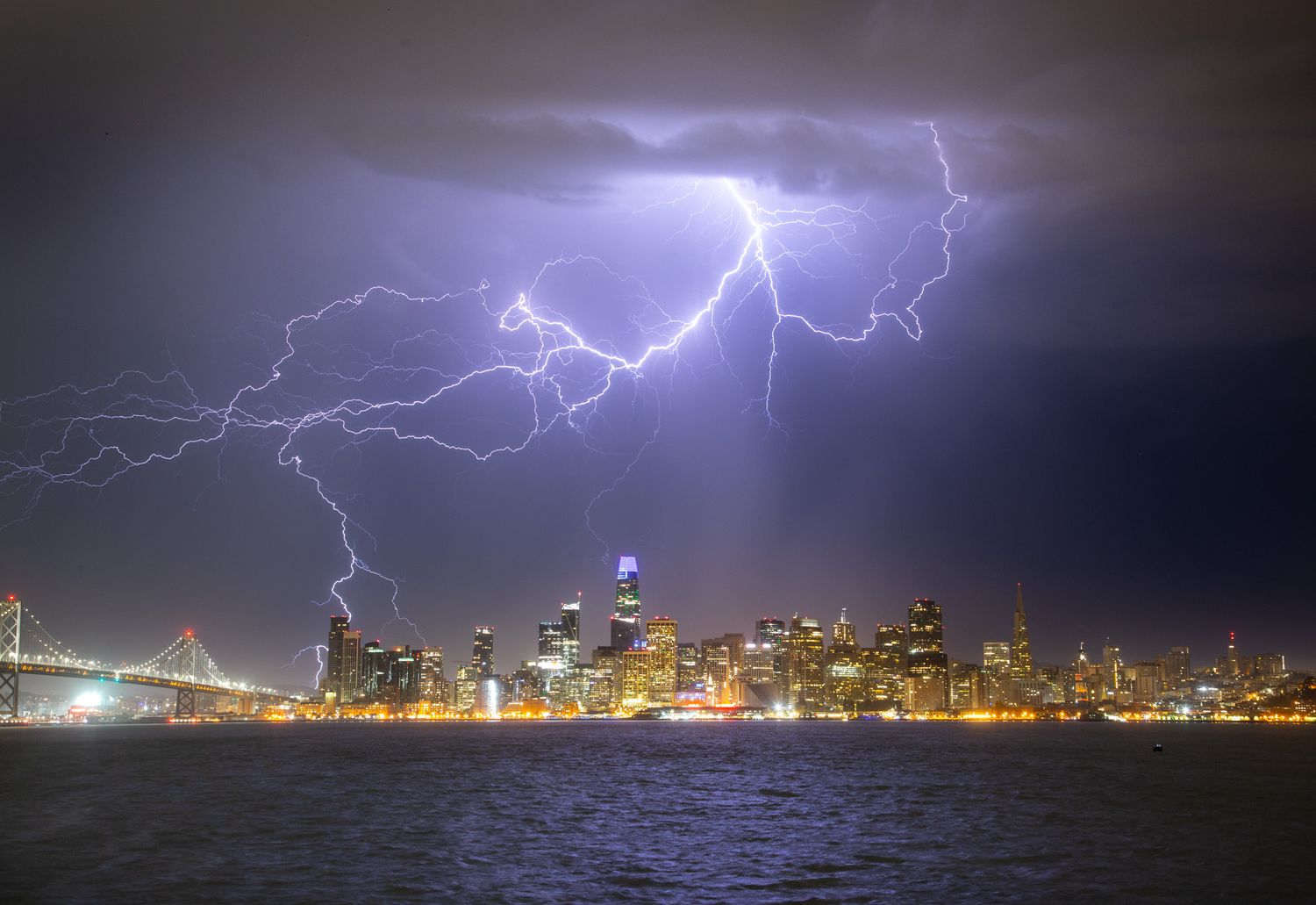 Dramatic lightning bolts streak across night sky above San Francisco's illuminated downtown skyline.