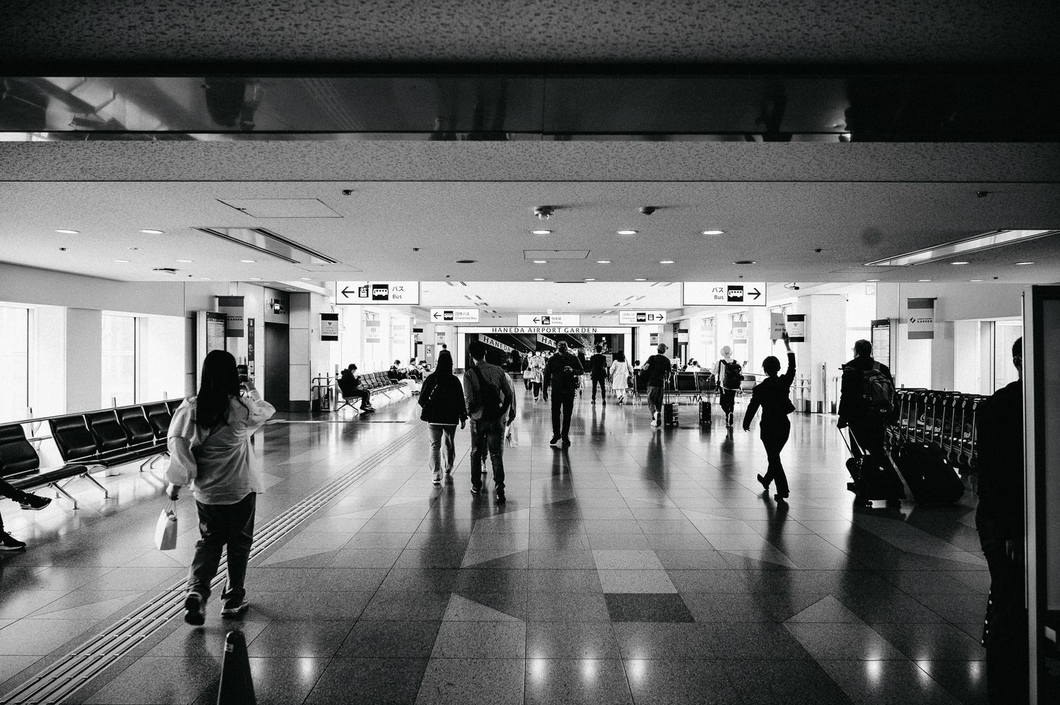 People walking through a bright airport terminal corridor with rows of seating.