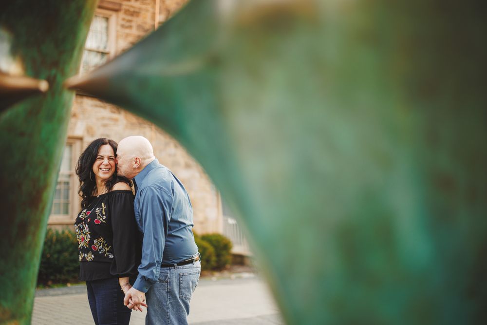 engaged couple smiling, laughing and holding hands through sculpture at Princeton University