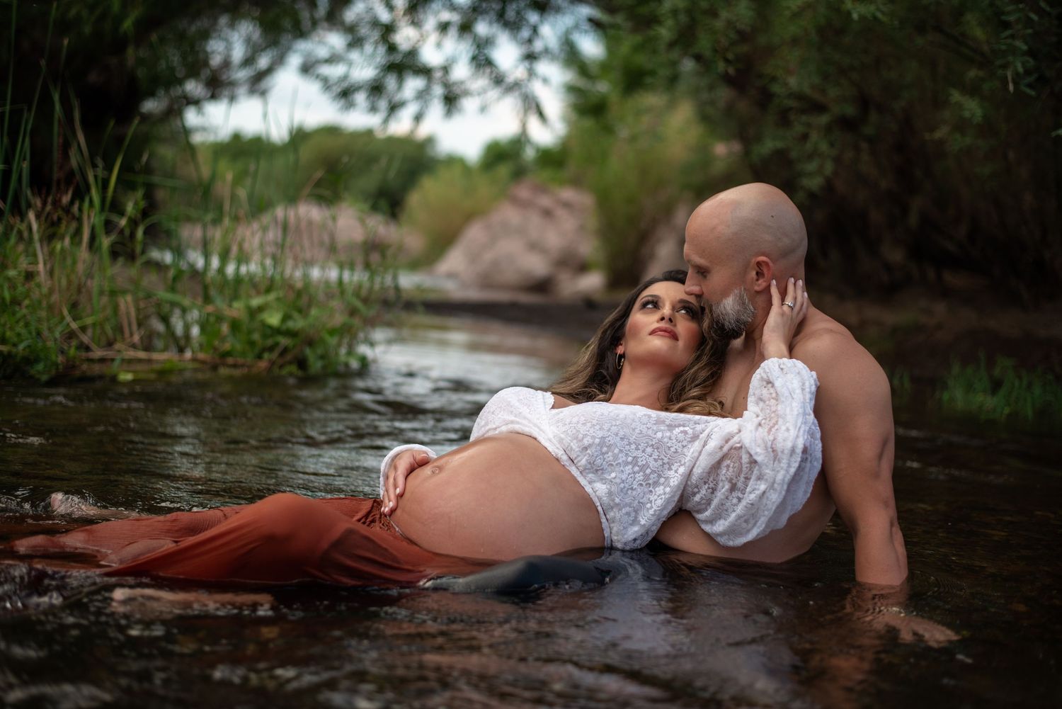 maternity couple photography session in water, shes laying in his lay looking back at him while he is staring down at her