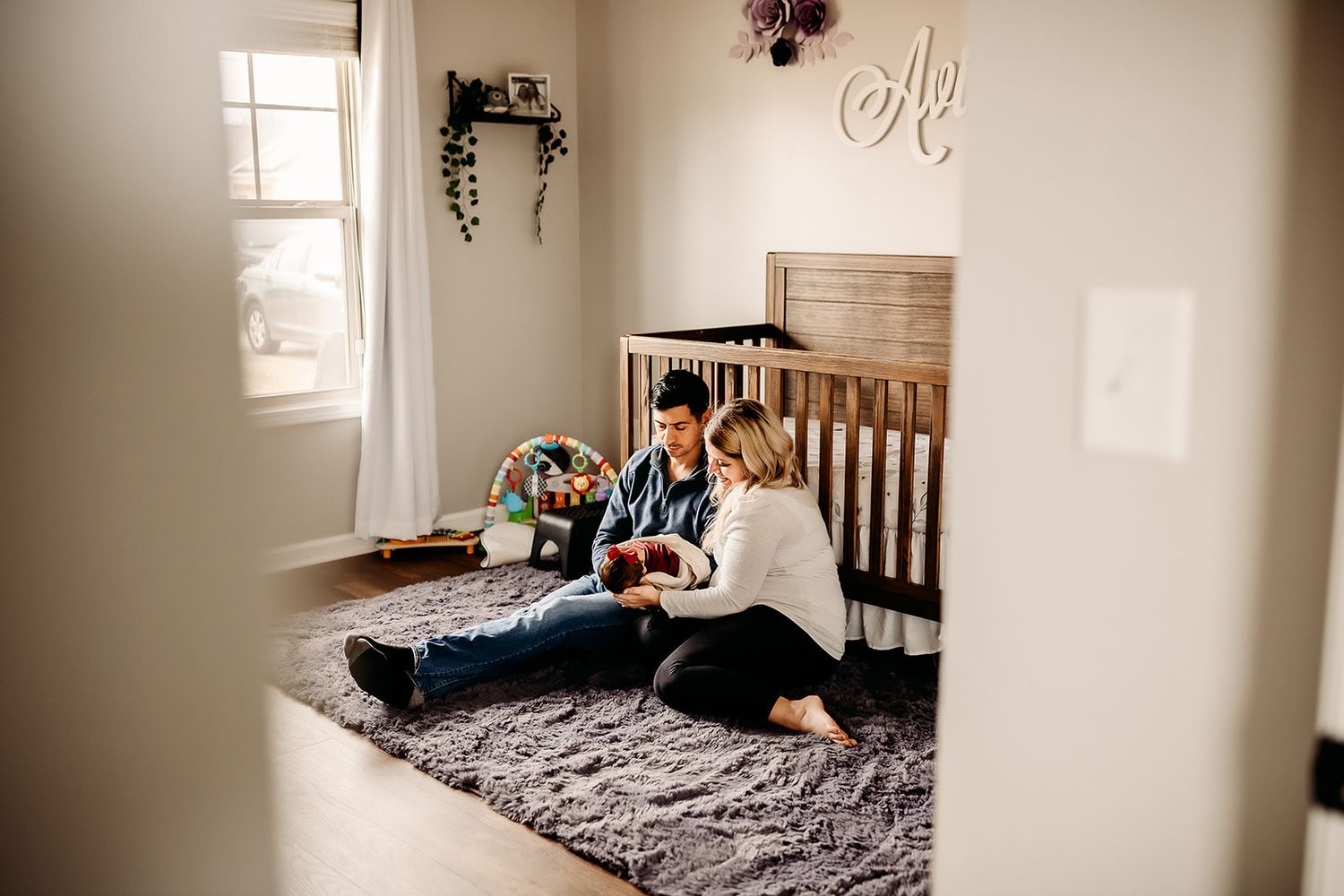 A wide angle view of parents sitting in front of their daughter's crib while gazing down at her.