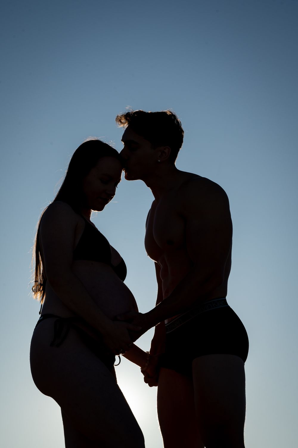 Sun silhouette of a pregnant mum and her husband