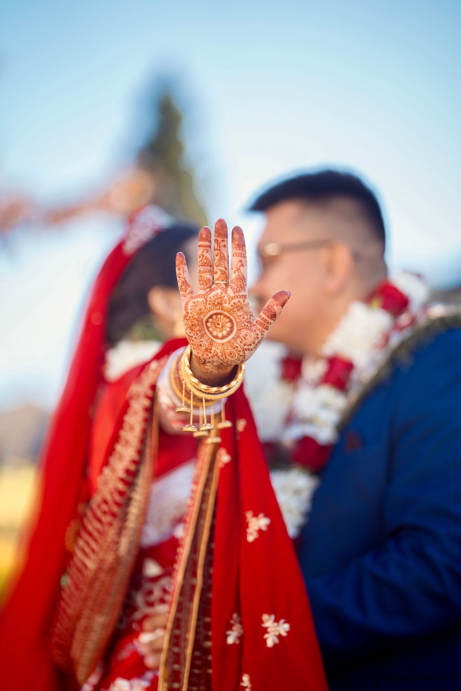 A beautifully decorated henna design displayed on a palm with wedding attire in the background.