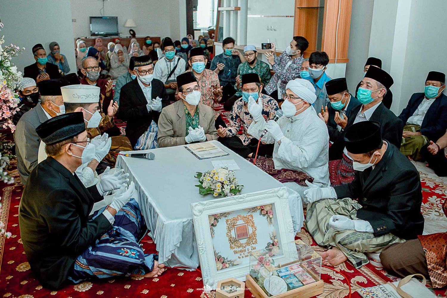 Large gathering of people in traditional dress and masks attending religious ceremony indoors.
