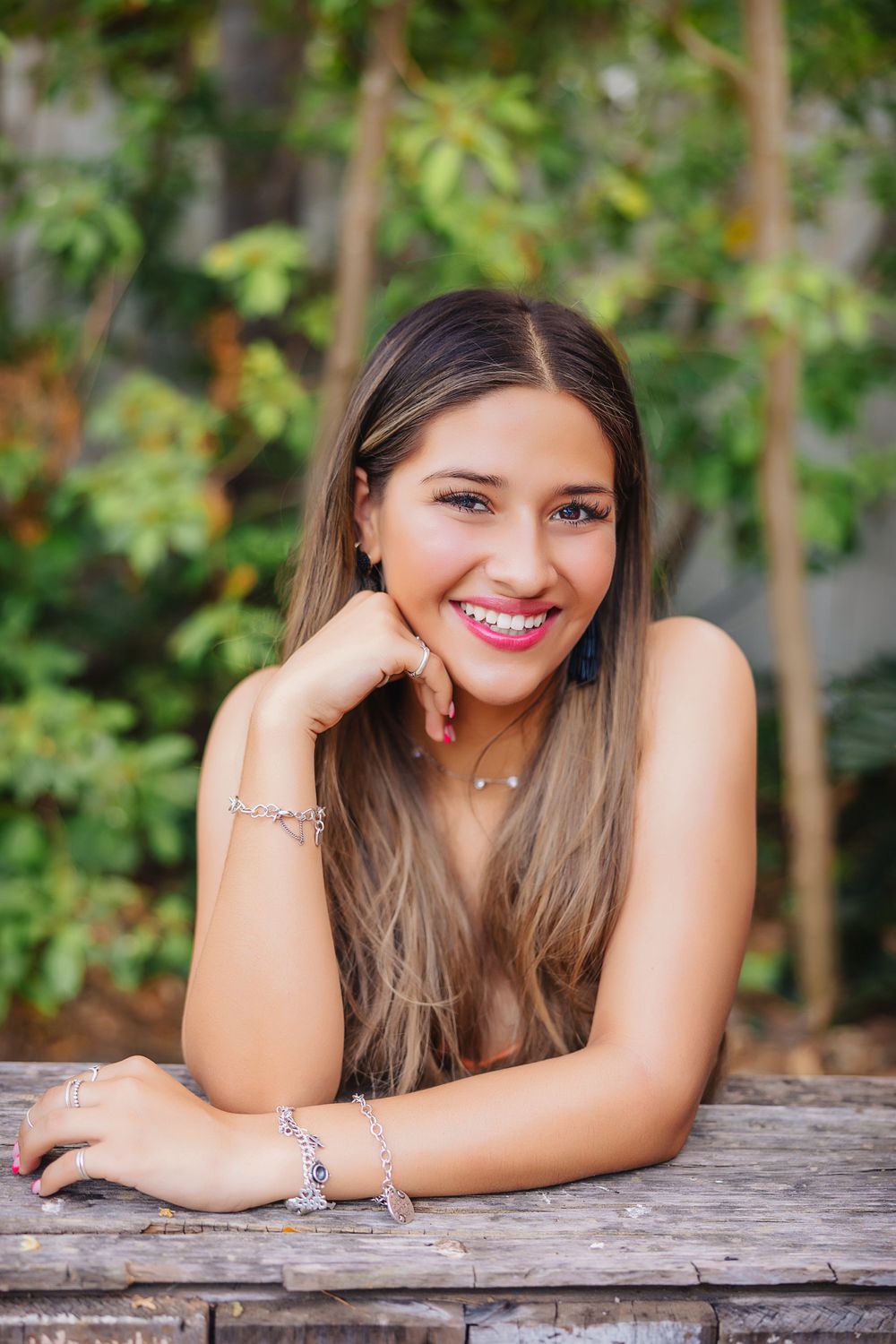 Outdoor portrait on wooden surface with natural greenery background and jewelry accessories.