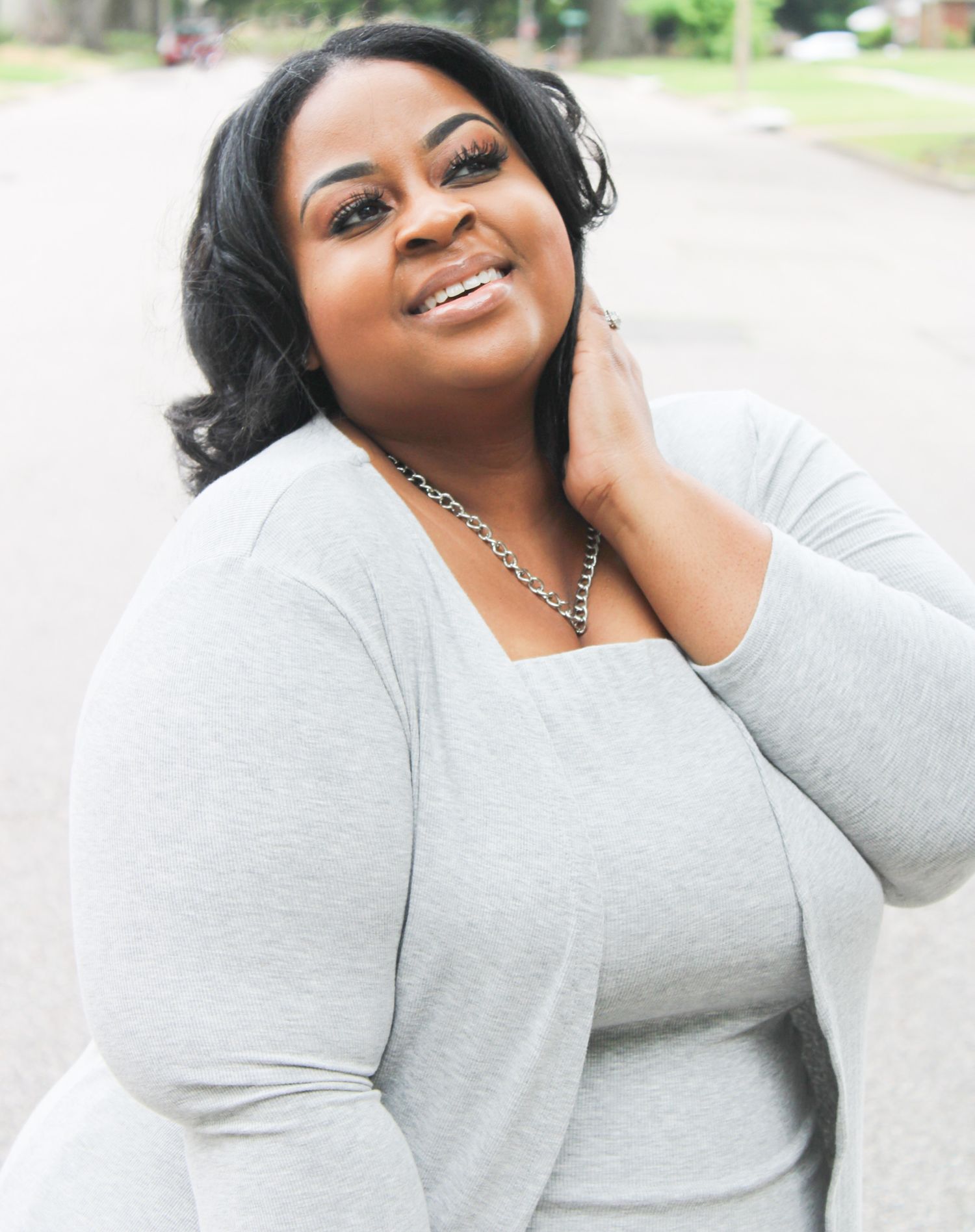 A portrait of a person in a light gray top smiling outdoors with natural lighting.