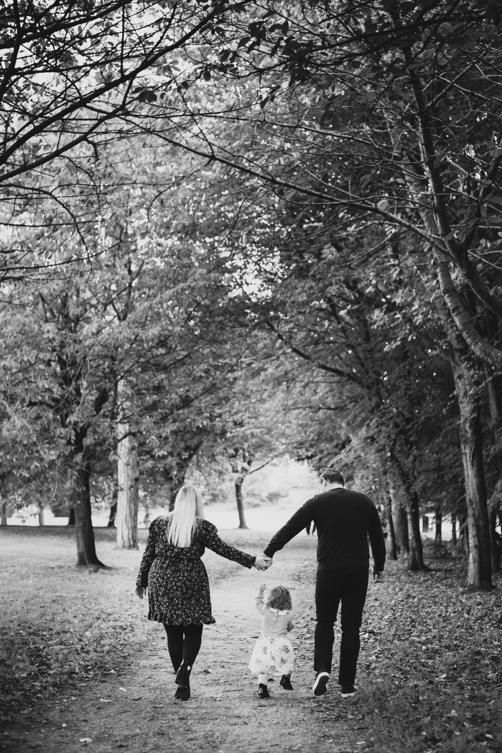 A black and white photo of a couple walking in Eastbourne park with their daughter for family photoshoot