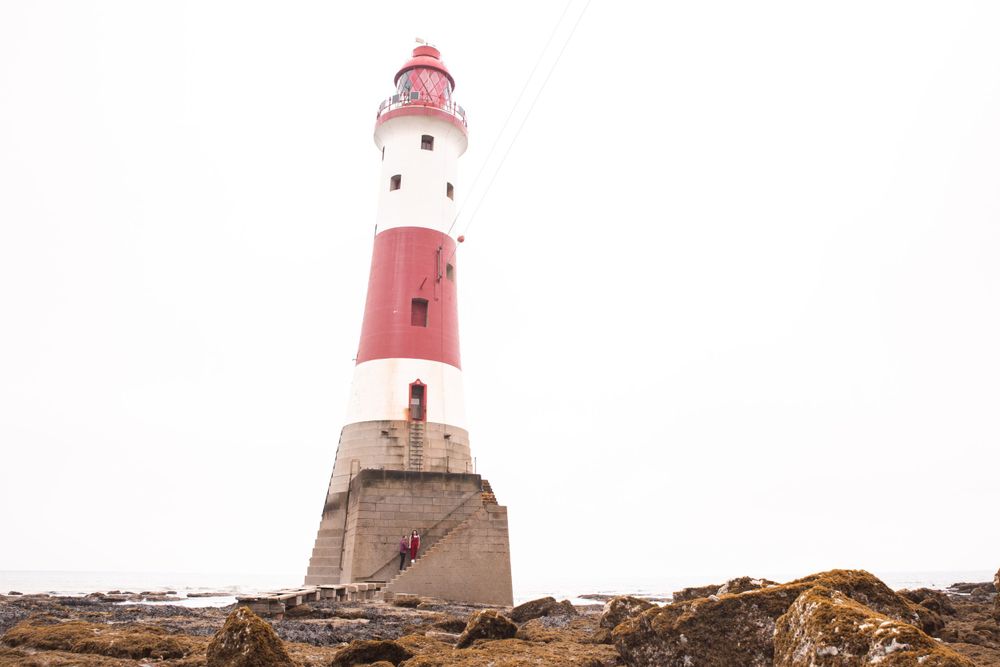 A landscape image of Beachy Head Lighthouse and a couple climbing the stairs for an engagement photoshoot in Eastbourne